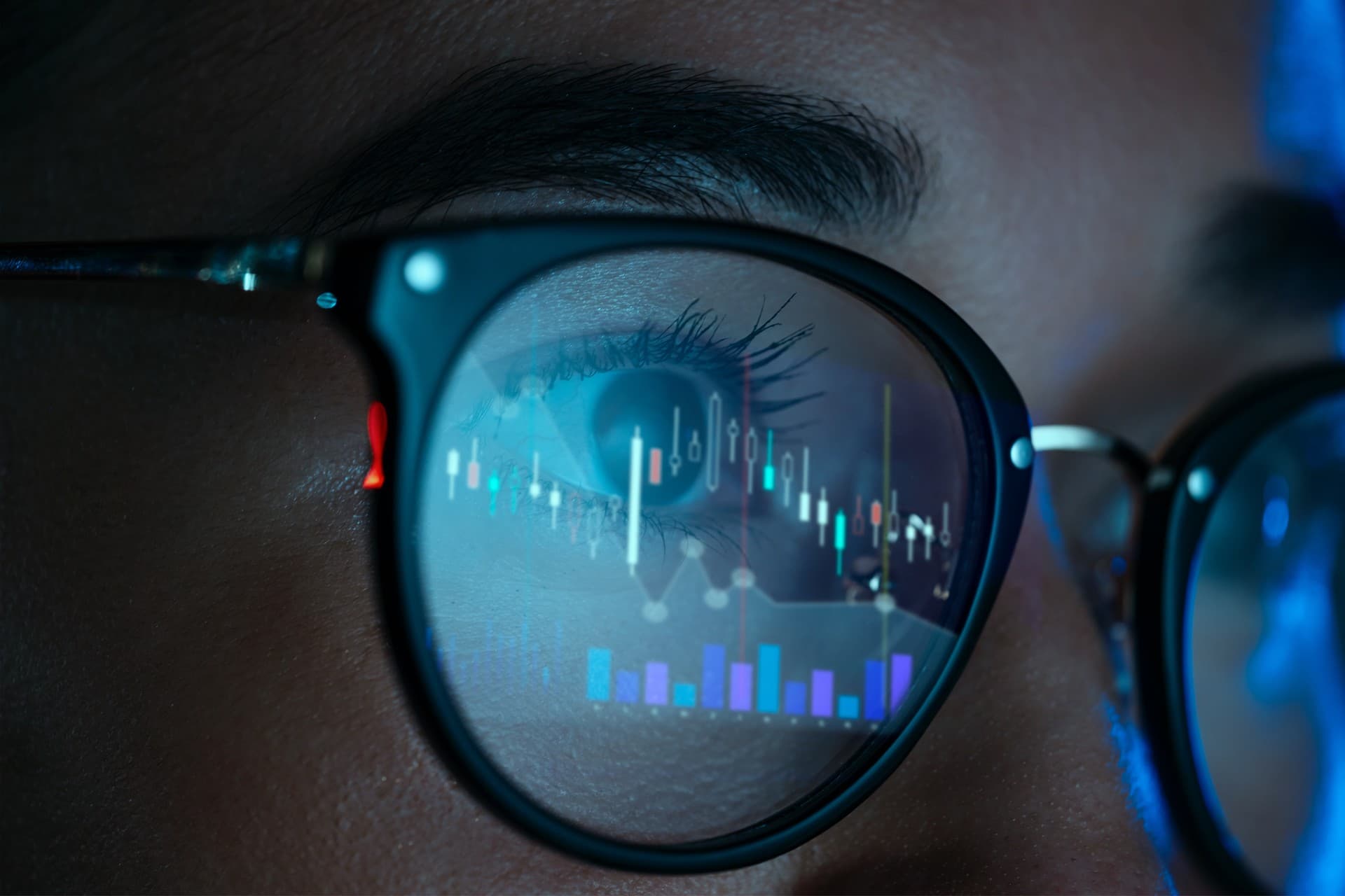 Close-up of a person wearing glasses reflecting stock market graphs and charts, focusing on financial data analysis.